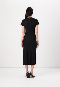 Black midi dress with short sleeves, featuring a subtle pattern, fitted silhouette, and a hem that falls below the knee. Worn with black heels.