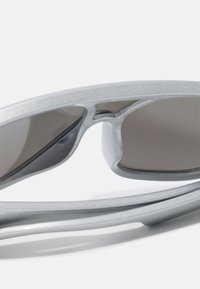 Lunettes de soleil avec une monture en plastique argenté élégant et des verres teintés foncés, présentant une texture lisse et un design épuré.