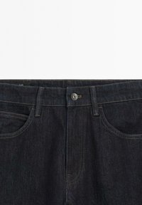 Donkerblauwe spijkerbroek met knoopsluiting, riemlussen en voorzakken, getoond tegen een witte achtergrond.