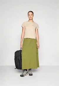 Camiseta beige corta, falda cargo verde, mochila negra, botas de senderismo grises. Cuenta con bolsillo en la camiseta, bolsillos en la falda y elementos de diseño prácticos.