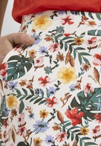 Tissu à imprimé floral présentant une variété de fleurs colorées, notamment des rouges, des jaunes et des violets, sur un fond blanc, avec des feuilles vertes.