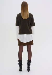 Pull en maille marron à manches courtes, chemise blanche en dessous, jupe marron, bottes noires à genoux en tissu flou et collants noirs transparents.