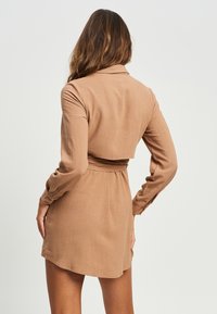 Rjavo oblečeno oblekico z dolgimi rokavi, ovratnikom, z zategnjeno pasom in prosto padajočim robom. Gladek material z subtilno teksturo in brez vidnih vzorcev.