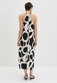 Schwarz- und cremefarbenes Neckholderkleid mit fließendem Design, abstrakten, kreisförmigen Mustern und einer Midi-Länge aus leichtem Stoff.