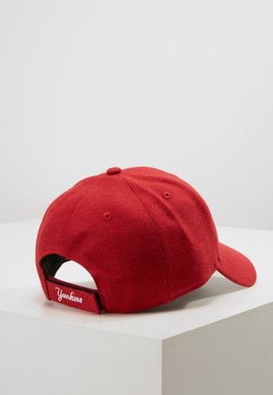 Red baseball cap with adjustable strap and "Yankees" embroidered in white on the back, placed on a white surface against a plain background.