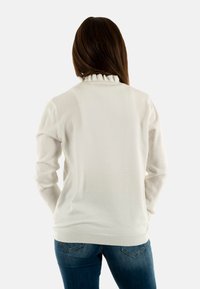 Pullover bianco a maglia con colletto arricciato; presenta un motivo a pois testurizzato; maniche lunghe; orlo aderente; abbinato a jeans blu.