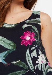 Canottiera nera con motivo floreale, caratterizzata da grandi fiori rosa e bianchi con foglie verdi, che mette in risalto un taglio rilassato e una texture del tessuto liscia.