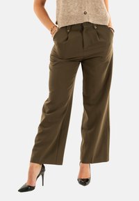 Pantaloni a gamba larga verde oliva realizzati in tessuto morbido, con pieghe frontali e due tasche laterali. Abbinati a tacchi alti neri.