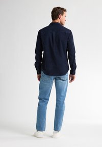 Donkerblauwe button-up shirt met een ruitpatroon, lange mouwen en een kraag. Gecombineerd met lichtblauwe jeans en witte sneakers.