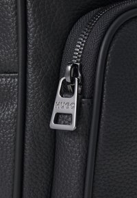 Borsa in pelle nera texture con un design elegante. Presenta una zip silver e un tirazip con logo per un accesso facile e una maggiore durabilità.