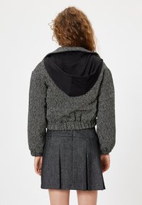 Avkortad herringbone-jacka i svart och vitt med en svart huvtröja. Elastisk nederkant och rynkade ärmar. Grå plisserad kjol.