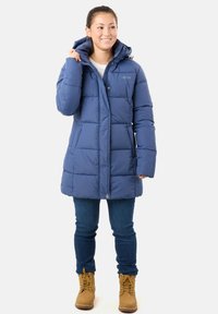 Blå puffjacka med huva, kviltad textur, framknappar och två sidofickor. Matchad med mörka jeans och bruna stövlar.