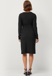 Zwarte midi-jurk met lange mouwen en een ronde hals. Glad stof, aansluitende taille en een rechte rok. Draag met sandalen op blokhak.