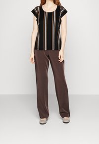 Top a rayas negras con mangas cortas tipo cap, que presenta rayas verticales multicolores. Combinado con pantalones marrones y zapatos grises.
