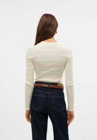 Maglione a coste crema con maniche lunghe, caratterizzato da righe orizzontali ad openwork. Abbinato a jeans in denim scuro a vita alta e una cintura marrone.