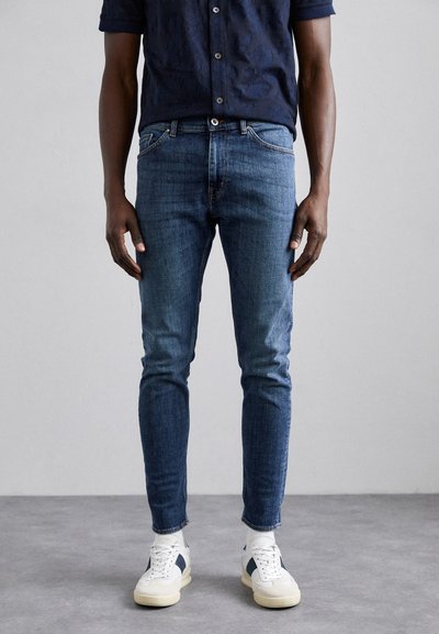 Jeans z denimu w średnim odcieniu niebieskiego, slim fit, z delikatnym wyblaknięciem i pięcioma kieszeniami, w połączeniu z białymi i granatowymi sneakersami.