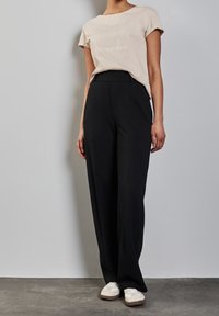 Ljusrosa t-shirt med texten "CONTENTMENT", kombinerad med högmidjade, löst sittande svarta byxor och beigea sneakers. Mjuk tyg och avslappnad design.