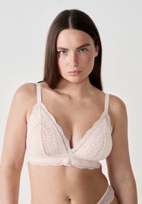 Bralette en dentelle rose clair avec une forme triangulaire, des bords festonnés, des motifs complexes et des bretelles réglables.