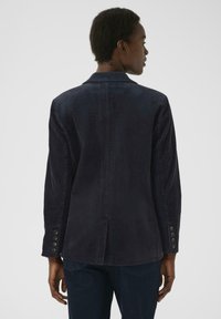Dunkelblaues Cordblazer mit tailliertem Schnitt, langen Ärmeln und Knöpfen an den Manschetten. Textil mit vertikalen Rippungen, Rückenschlitzdetail.