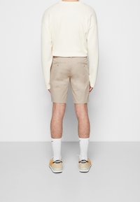 Beige korte broek, ribbelige crèmekleurige trui, witte sokken en lichte schoenen. Bevat subtiele achterzakken op de korte broek, wat een casual uitstraling geeft.