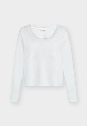 Witte cropped top met lange mouwen en een ronde hals, getoond op een effen lichtgrijze achtergrond.