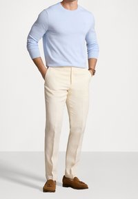 Jasnoniebieski sweter z dzianiny, kremowe lniane spodnie oraz brązowe zamszowe mokasyny. Sweter ma długie rękawy; spodnie są dopasowane i mają prostą nogawkę.