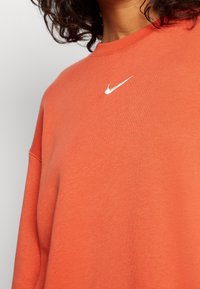 Orange sweatshirt i bomullsmix, med rund hals och en liten, vit broderad Nike-logotyp på bröstet. Avslappnad passform.