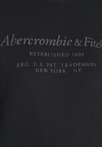 Sudadera negra con texto en relieve: "Abercrombie & Fitch Establecido en 1892" e información de marca registrada en gris. Textura de tejido suave.