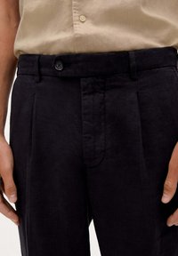 Dunkelblaue Leinenhose mit maßgeschneidertem Schnitt, ausgestattet mit einem Knopfverschluss, gefältelter Vorderseite und leichter Textur.