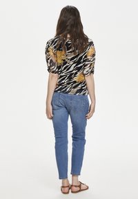 Blusa a fantasia nera e beige con dettagli floreali, maniche a palloncino, abbinata a jeans di denim azzurro chiaro e sandali marroni, vista da dietro.