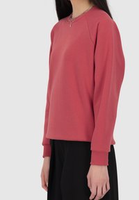 Sudadera roja de manga larga, confeccionada con una suave mezcla de algodón, cuello redondo, puños acanalados y un corte ligeramente oversize.