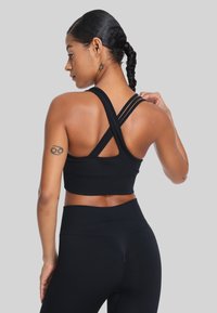 Zwarte sportieve crop top met een aansluitend ontwerp, kruisbanden op de rug en naadloze constructie. Gladde textuur zonder zichtbare hardware of patronen.