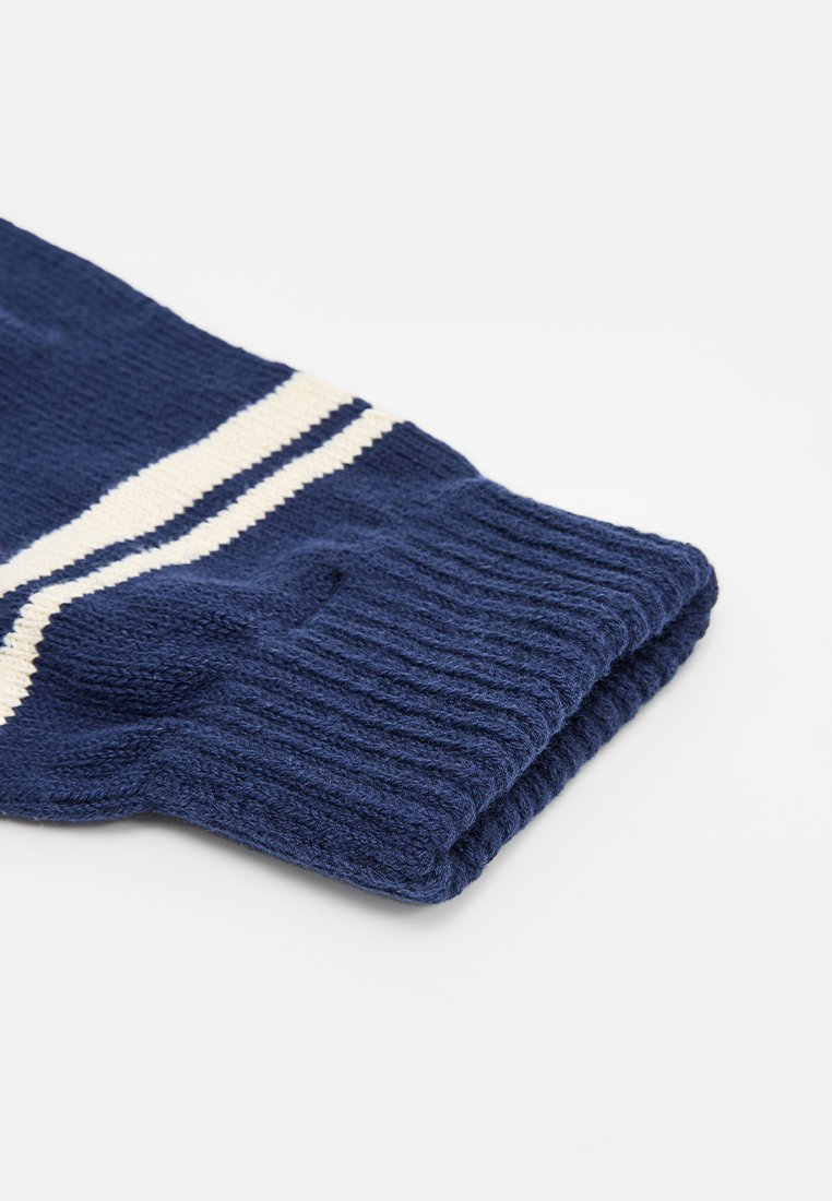 Navyblaue gestrickte Ärmel mit einer gerippten Textur, die zwei weiße horizontale Streifen zeigt. Das Material wirkt dick und gemütlich.