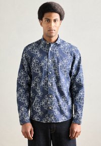 Πουκάμισο σε ναυτικό μπλε με λευκή κεντητή λουλουδάτη διακόσμηση, κούμπωμα με κουμπιά μπροστά και μακριά μανίκια· το ύφασμα φαίνεται υφασμένο με χαλαρή εφαρμογή.