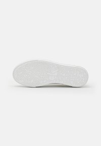 Suola di sneaker bianca con motivo in gomma testurizzata, caratterizzata da un logo stampato al centro e un design pulito e piatto.