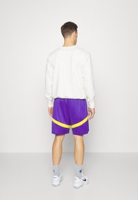 Vit långärmad sweatshirt kombinerad med lila shorts med gula detaljer. Shortsen har ett texturerat mönster och elastisk midja.