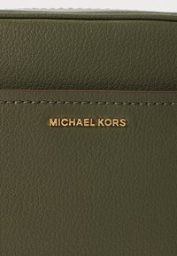 Zielony portfel z teksturowanej skóry z złotym logo "MICHAEL KORS", z subtelnym przeszyciem i kontrastowymi detalami wzdłuż krawędzi.