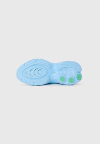 Semelle de sneaker bleue avec des motifs de crans incurvés et trois éléments circulaires verts près du talon sur un fond blanc uni.