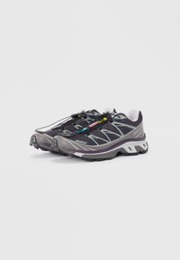 Leichte Outdoorschuhe aus Mesh und Gummi. Dunkelgrau mit reflektierenden Akzenten, Schnellschnürsystem und strukturierten Sohlen für besseren Halt.
