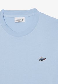 Lichtblauwe katoenen T-shirt met ronde hals, voorzien van een klein geborduurd krokodillen logo. Klassieke pasvorm met een geribbelde kraag en een zachte textuur.