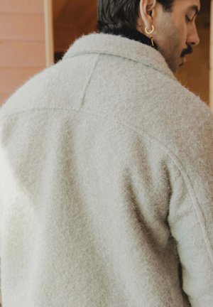 Veste en laine texturée gris clair avec un col classique, des détails de couture visibles et une coupe décontractée, vue de dos.