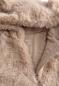 Kunstpels beige jakke med en blød inderside. Har en hætte og et lysebrunt for, der er markeret med brand- og størrelsesoplysninger.