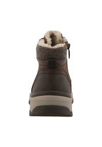 Botín marrón hasta el tobillo con un upper texturizado, forro de forro polar y cierre lateral, presentando una suela de goma resistente y un tacón beige en contraste.