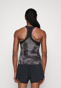 Camiseta sin mangas atlética negra con patrones gráficos texturizados y acentos rosas. Combinada con pantalones cortos oscuros, mostrando un diseño de espalda nadadora.