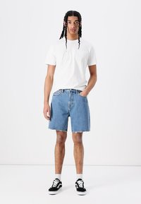 Shorts din denim albastru cu un finisaj decolorat, având un croi drept, tiv desfăcut și buzunare laterale, asortați cu un tricou alb simplu și teniși negri.