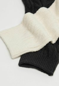 Szydełkowany szalik w czarno-kremowej kolorystyce, z prążkowaną i puszystą teksturą, prezentujący przytulny, warstwowy design.