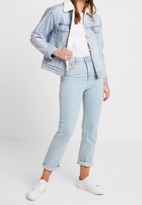 Jasnoniebieska kurtka dżinsowa z kołnierzem z materiału sherpa, ozdobiona kwiatowym haftem na rękawach. Noszona z jasnoniebieskimi jeansami ze zwiniętymi nogawkami i białymi trampkami.