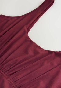 Burgunderrotes Kleid mit dünnen Trägern, das eine glatte Stofftextur und geraffte Details an der Brust aufweist.