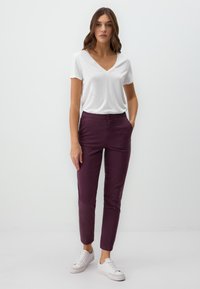 T-shirt blanc à col en V associé à un pantalon bordeaux ajusté et des baskets blanches. La tenue présente un design simple et une texture lisse.