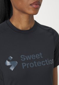 Svart treningstrøye med korte ermer, med en blank "Sweet Protection" logo på brystet, glatt tekstur og minimalistisk design.